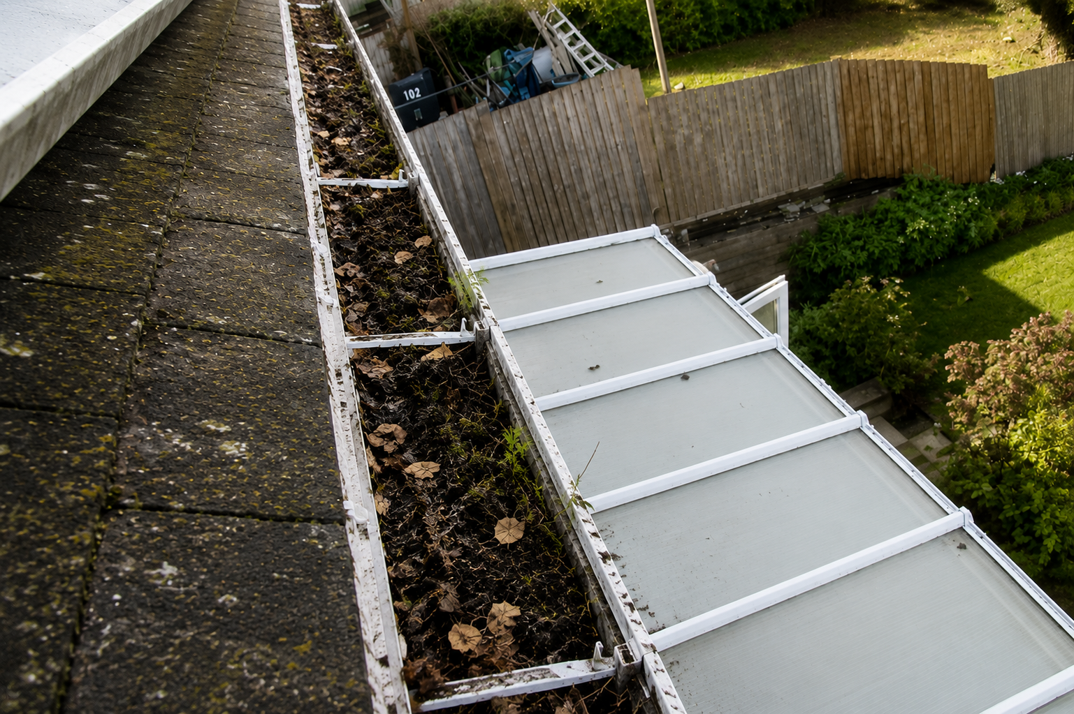 Before professional gutter cleaning showing compacted silt, organic debris, and moss buildup slowing drainage