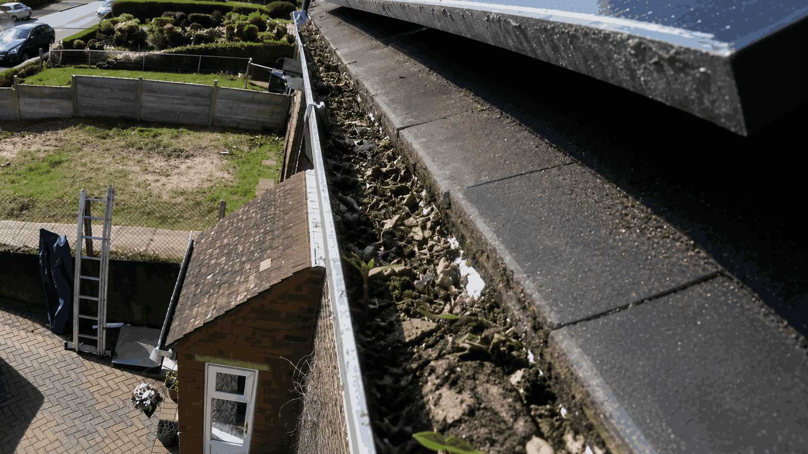 Heavily clogged gutter run before cleaning showing silt, leaves, and overflow staining