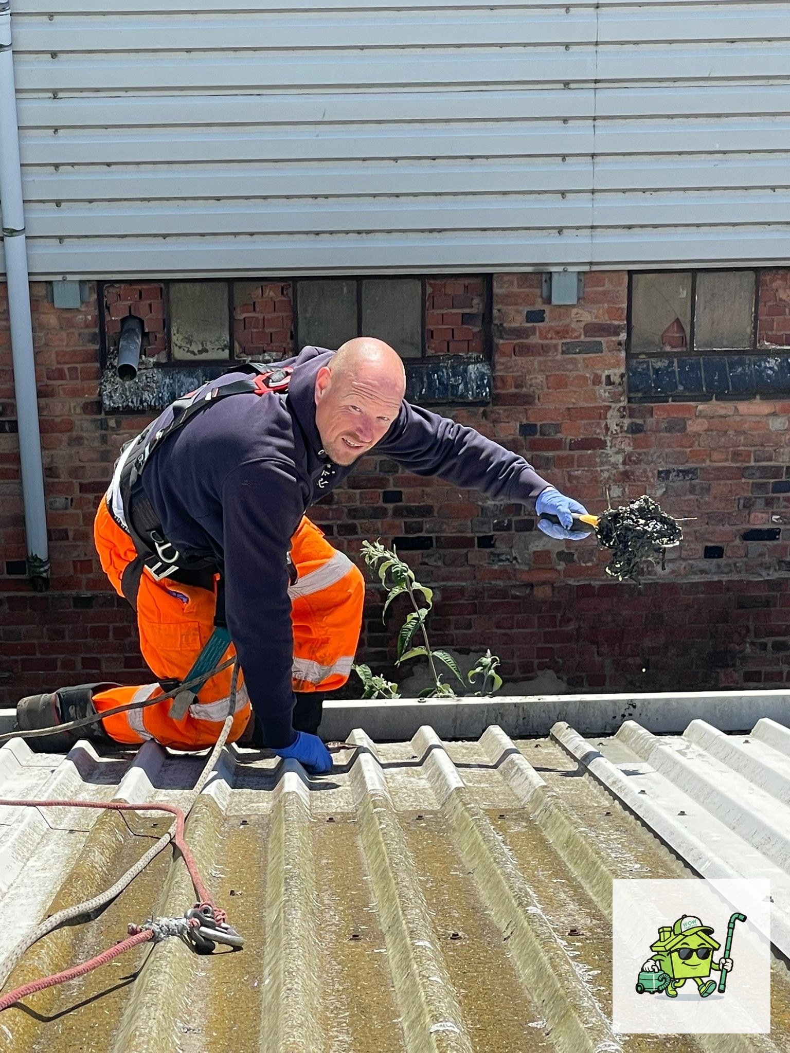 Commercial gutter debris removal in progress on Birmingham warehouse roof by harnessed operative